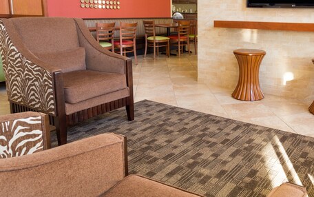 A hotel lobby with a seating area, a flat-screen TV mounted on the wall, and a patterned rug on the floor.