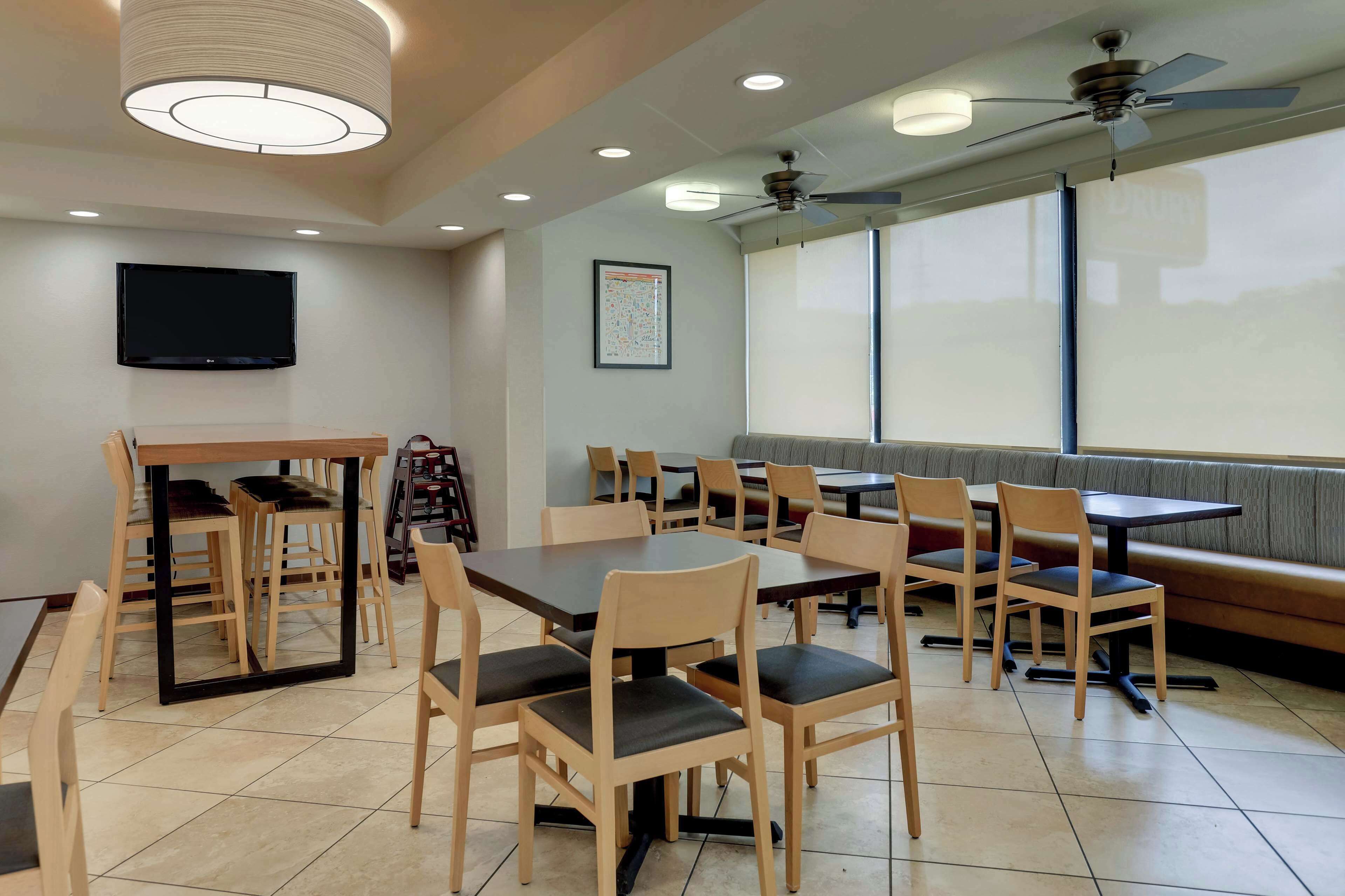 A dining area with tables and chairs, a television, ceiling fans, and large windows.