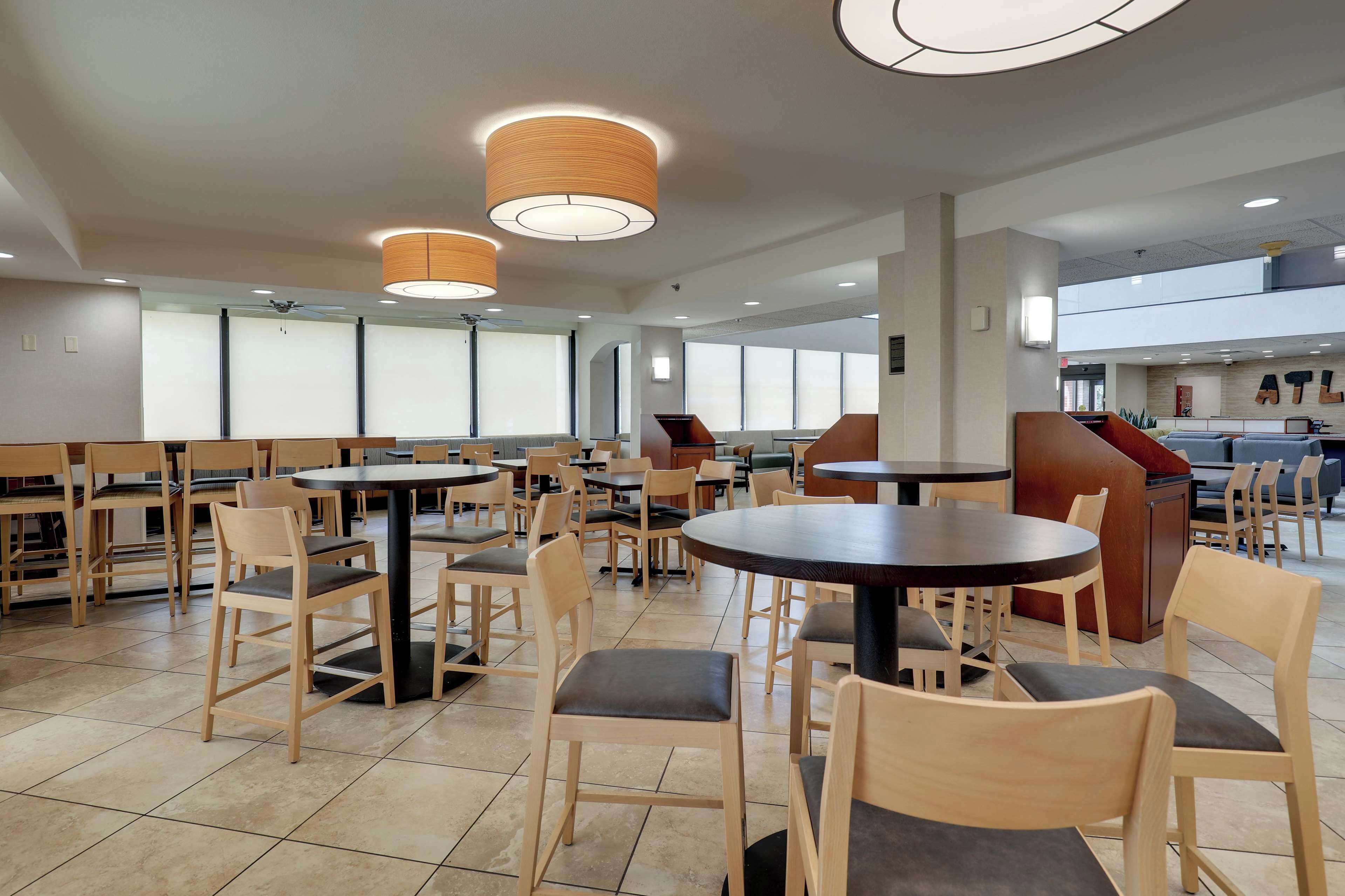 Un amplio comedor interior con varias mesas y sillas redondas, ventiladores de techo y grandes ventanales que dejan entrar luz natural.