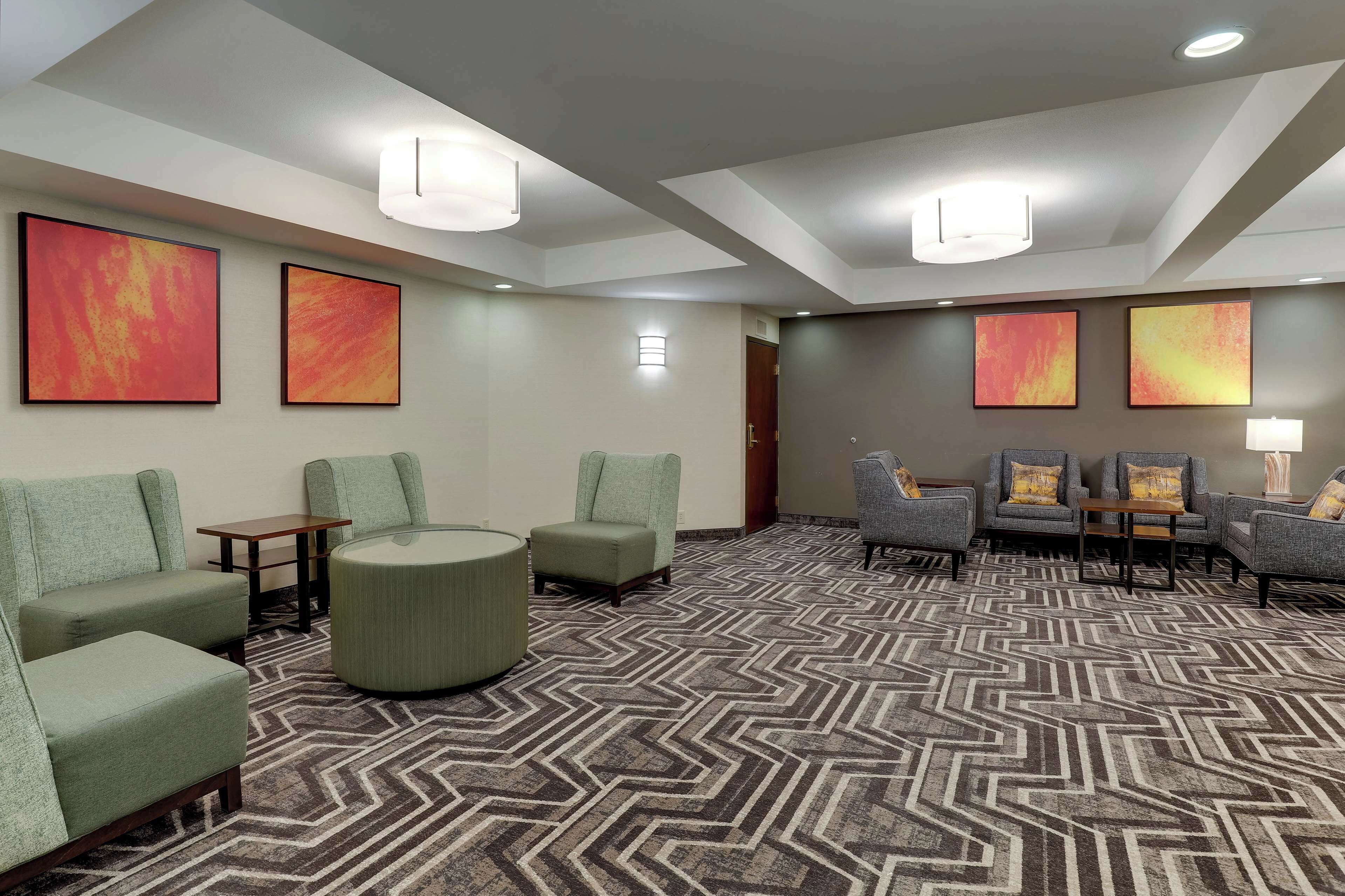 Un vestíbulo de hotel con diseño moderno, que presenta una alfombra estampada, varias zonas de estar con sillones y sofás, y obras de arte en las paredes.