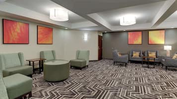 Un vestíbulo de hotel con diseño moderno, que presenta una alfombra estampada, varias zonas de estar con sillones y sofás, y obras de arte en las paredes.
