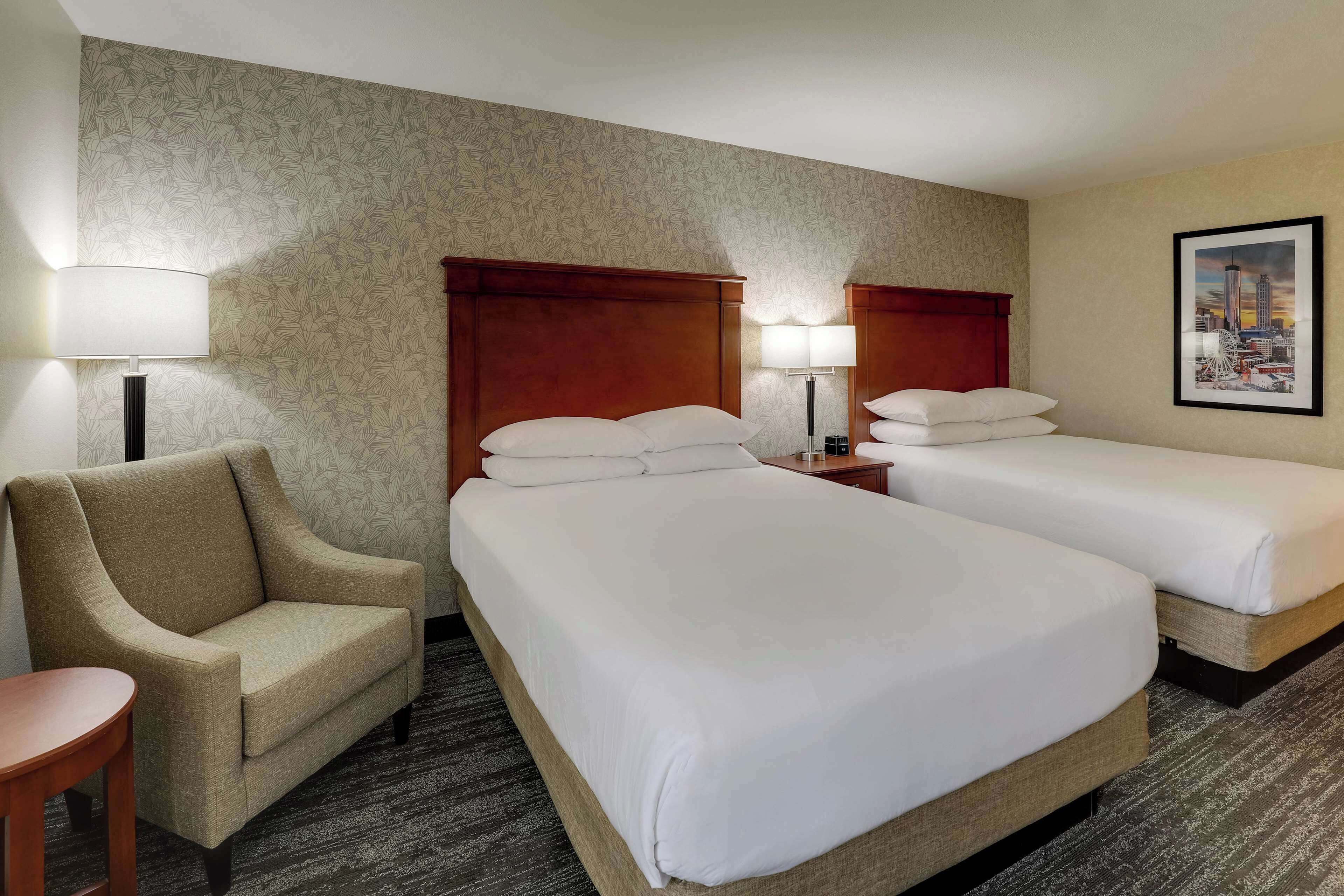 Ein Hotelzimmer mit zwei Betten, einem Sessel, einer Lampe und einem gerahmten Bild an der Wand.