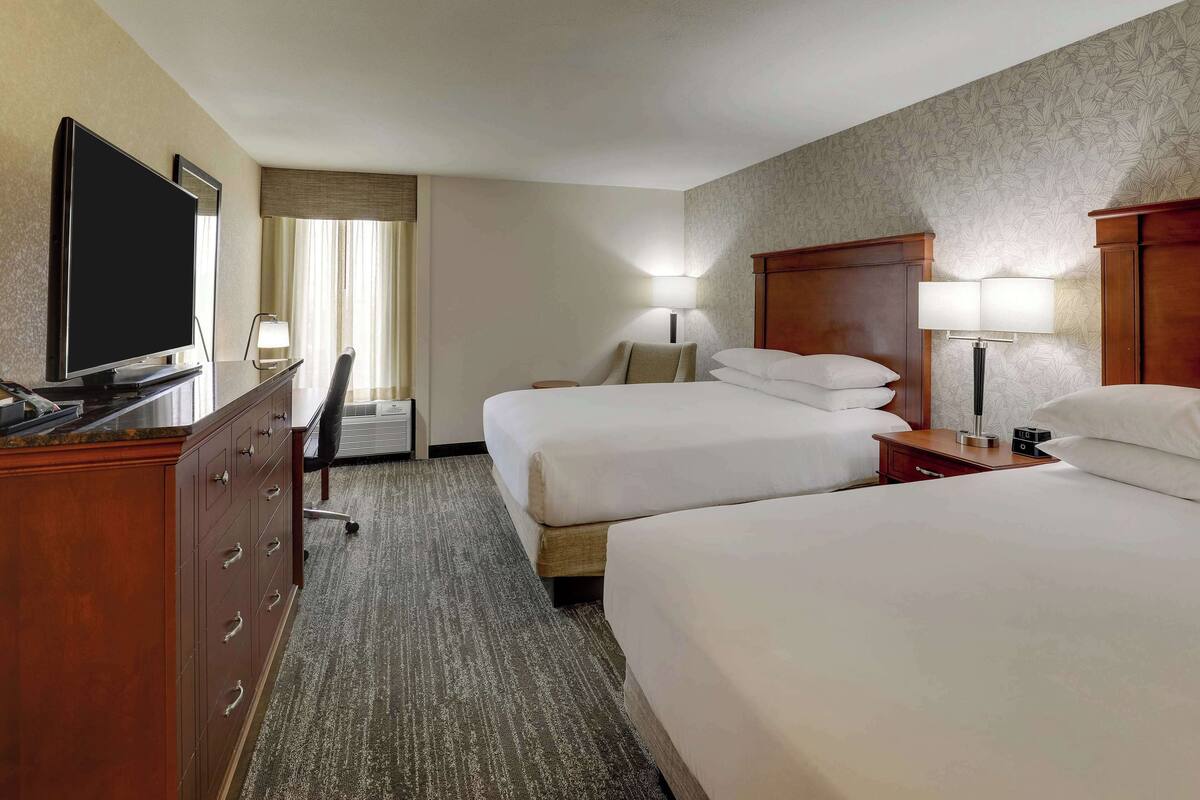 A hotel room with two beds, a desk with a television, a lamp, and a dresser.
