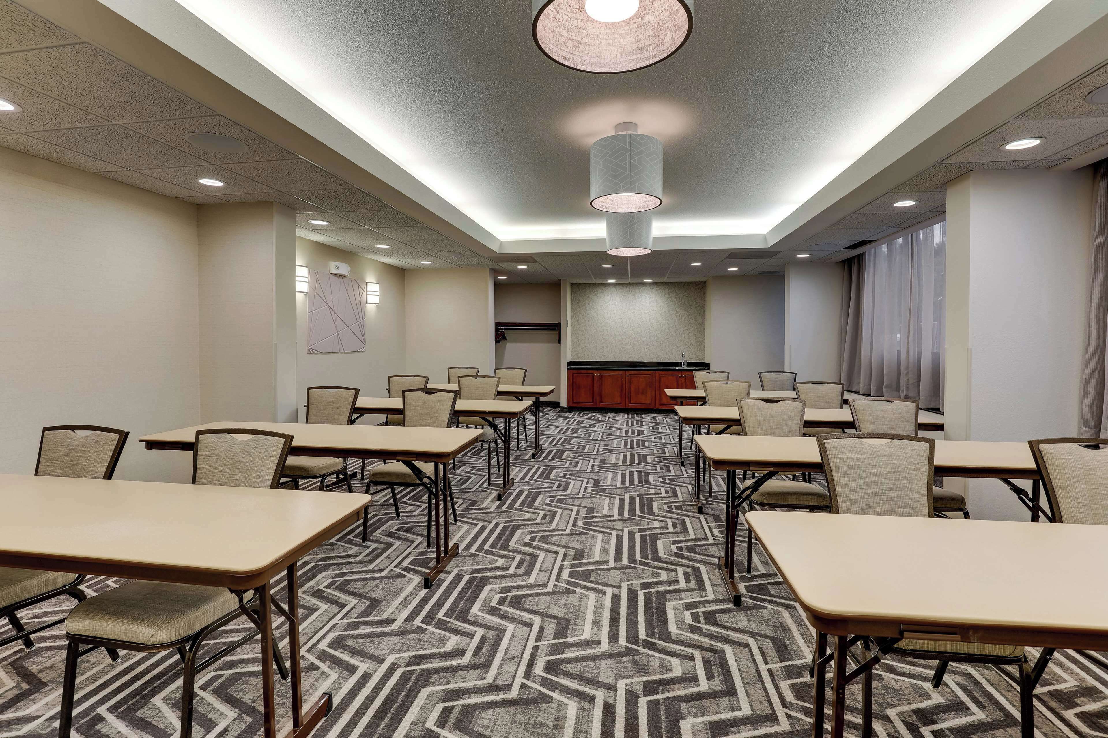 A conference room with multiple tables and chairs, a patterned carpet, and a large chandelier.