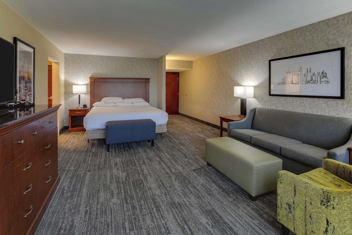 A hotel room with a large bed, a sofa, a desk, and a TV.