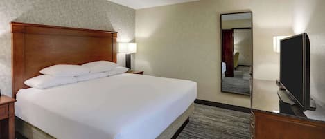 Een hotelkamer met een groot bed, een houten hoofdbord, een nachtkastje, een lamp, een flatscreen televisie en een spiegel aan de muur.