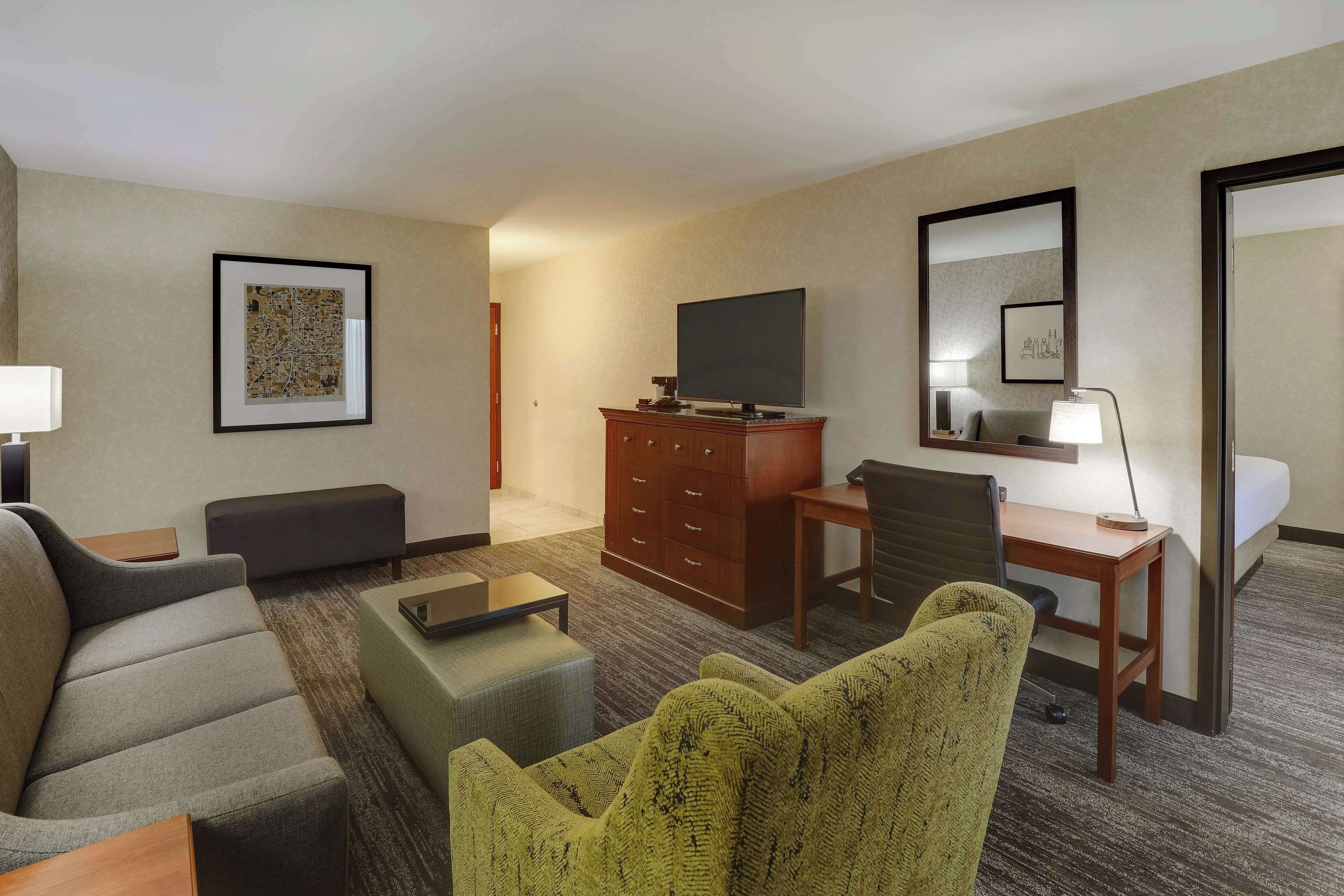 Habitación de hotel con sofá, sillón, escritorio, televisión y cama.