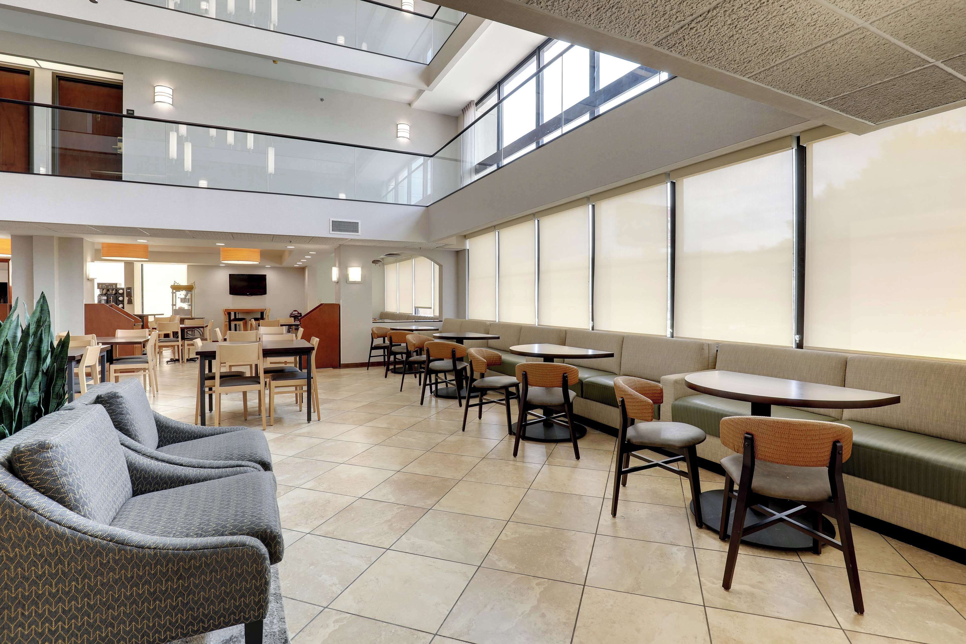 A spacious indoor area with multiple seating options including sofas, chairs, and tables, a television mounted on the wall, and large windows allowing natural light.