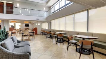 A spacious indoor area with multiple seating options including sofas, chairs, and tables, a television mounted on the wall, and large windows allowing natural light.