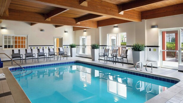 An indoor swimming pool with a tiled edge, wooden ceiling beams, and several lounge chairs and potted plants around the pool area. - Fairfield Inn & Suites by Marriott Denver Airport (Denver)