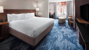 A hotel room with a large bed, a desk, a TV, and a seating area with a view of the outdoors. - Fairfield Inn & Suites by Marriott Denver Airport (Denver)