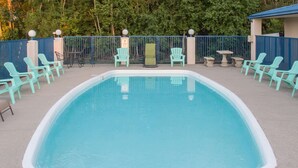 Een rechthoekig zwembad met een witte rand, omringd door turquoise stoelen en tafels.