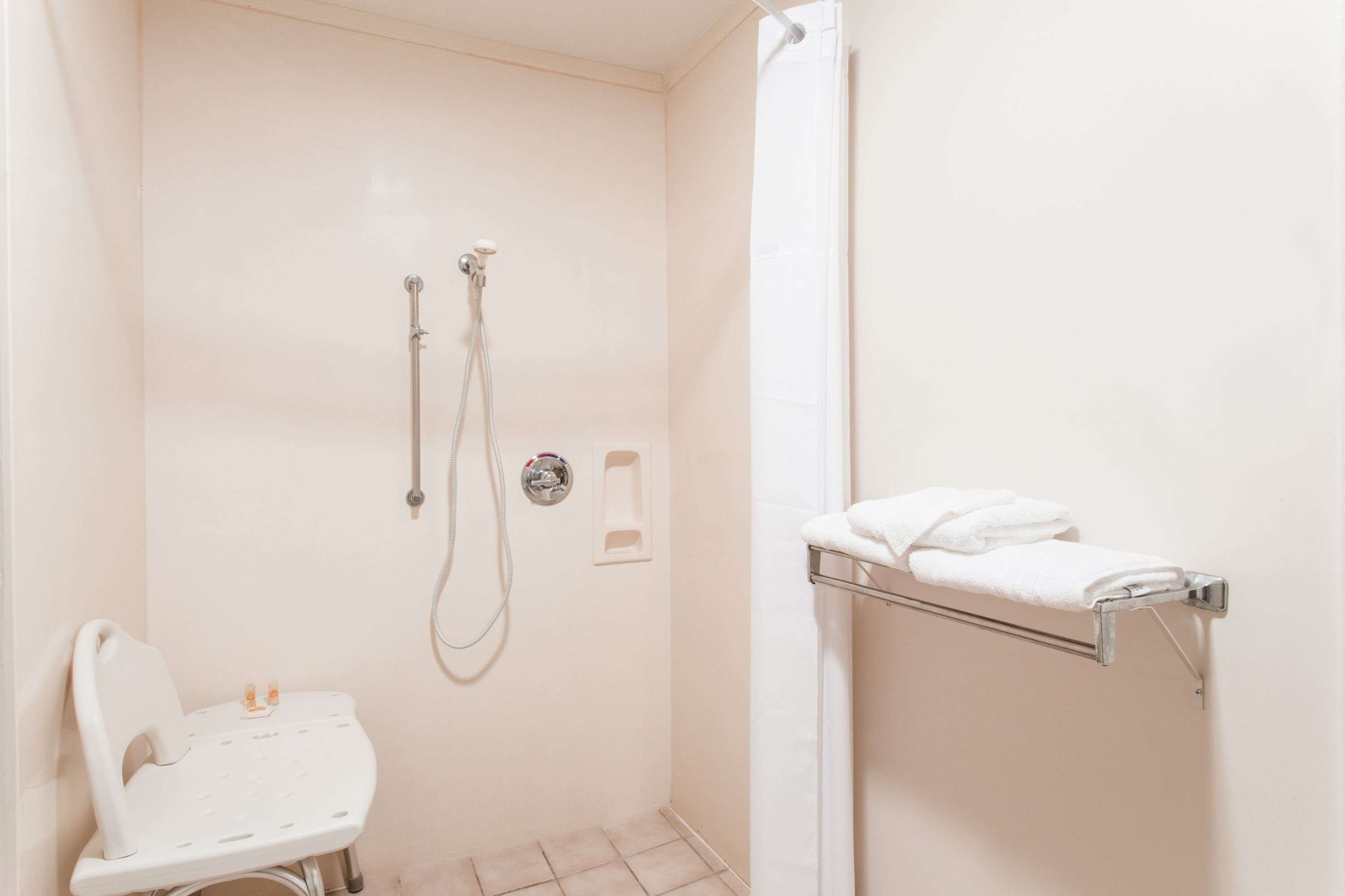 A small, white bathroom with a shower, a toilet, and a towel rack.