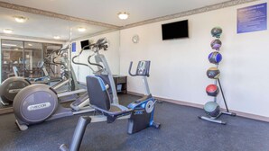 Een sportschool met trainingsapparatuur, een spiegel en een aan de muur bevestigde televisie.