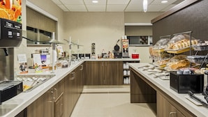 A modern kitchen area with a self-service station, including a coffee machine, a waffle maker, and a variety of food items.