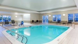 An indoor swimming pool with clear water, surrounded by lounge chairs and a sunbed, with large windows on one side.