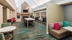 A hotel lobby with a high ceiling, a fireplace, a dining area, and a seating area with a sofa and chairs.
