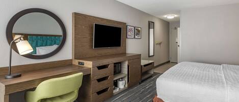 A hotel room with a bed, a desk with a chair, a television, a mirror, and a door.
