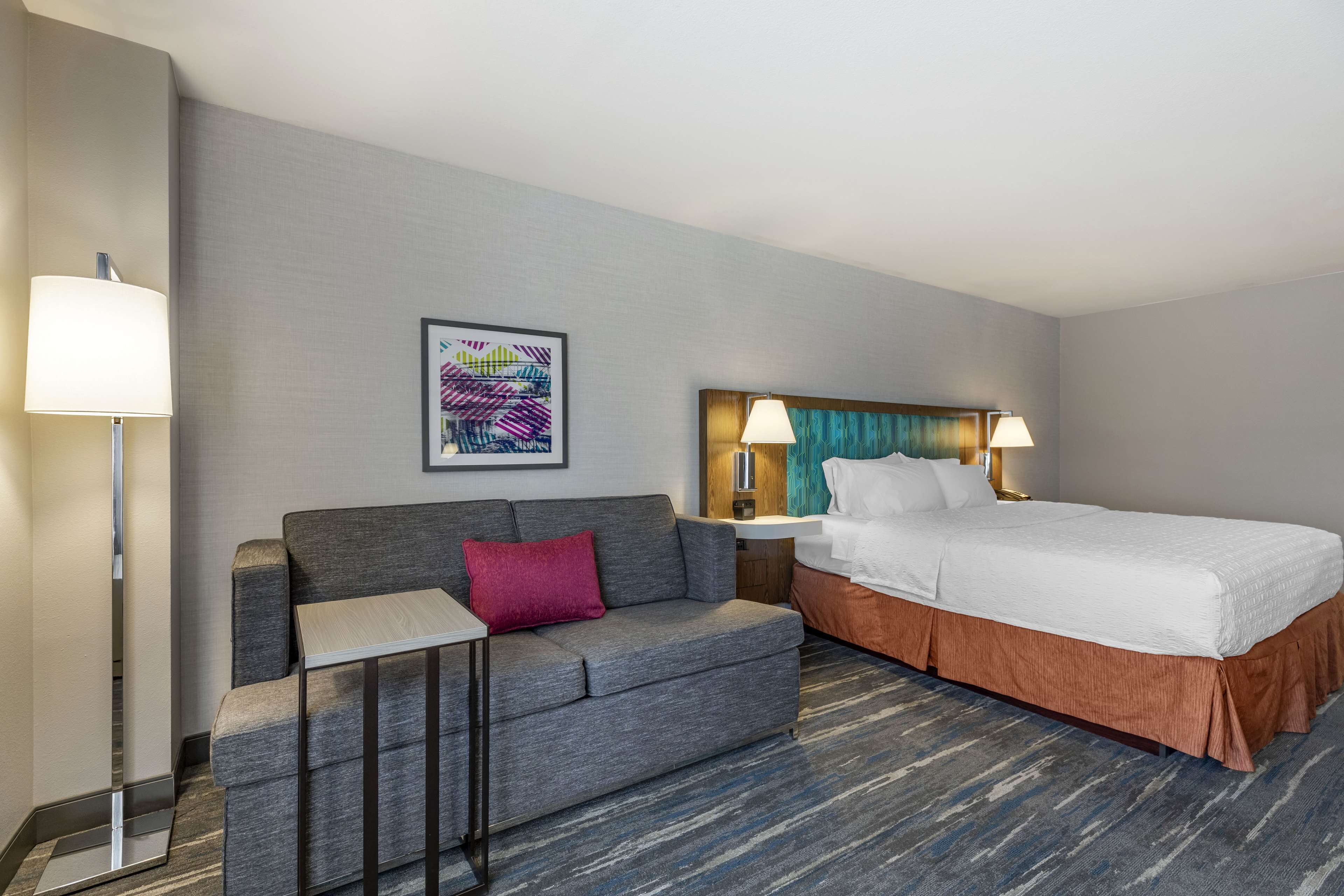 Ein Hotelzimmer mit Bett, Sofa, kleinem Tisch und Nachttisch mit Lampen.