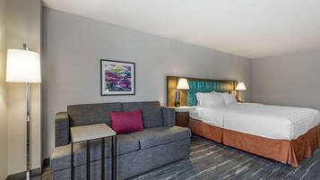 A hotel room with a bed, a sofa, a small table, and a nightstand with lamps.