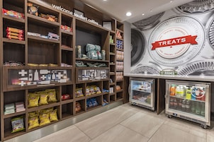 Zona de exhibición de aperitivos y bebidas, con estantes llenos de diferentes opciones y una sección refrigerada con refrescos.