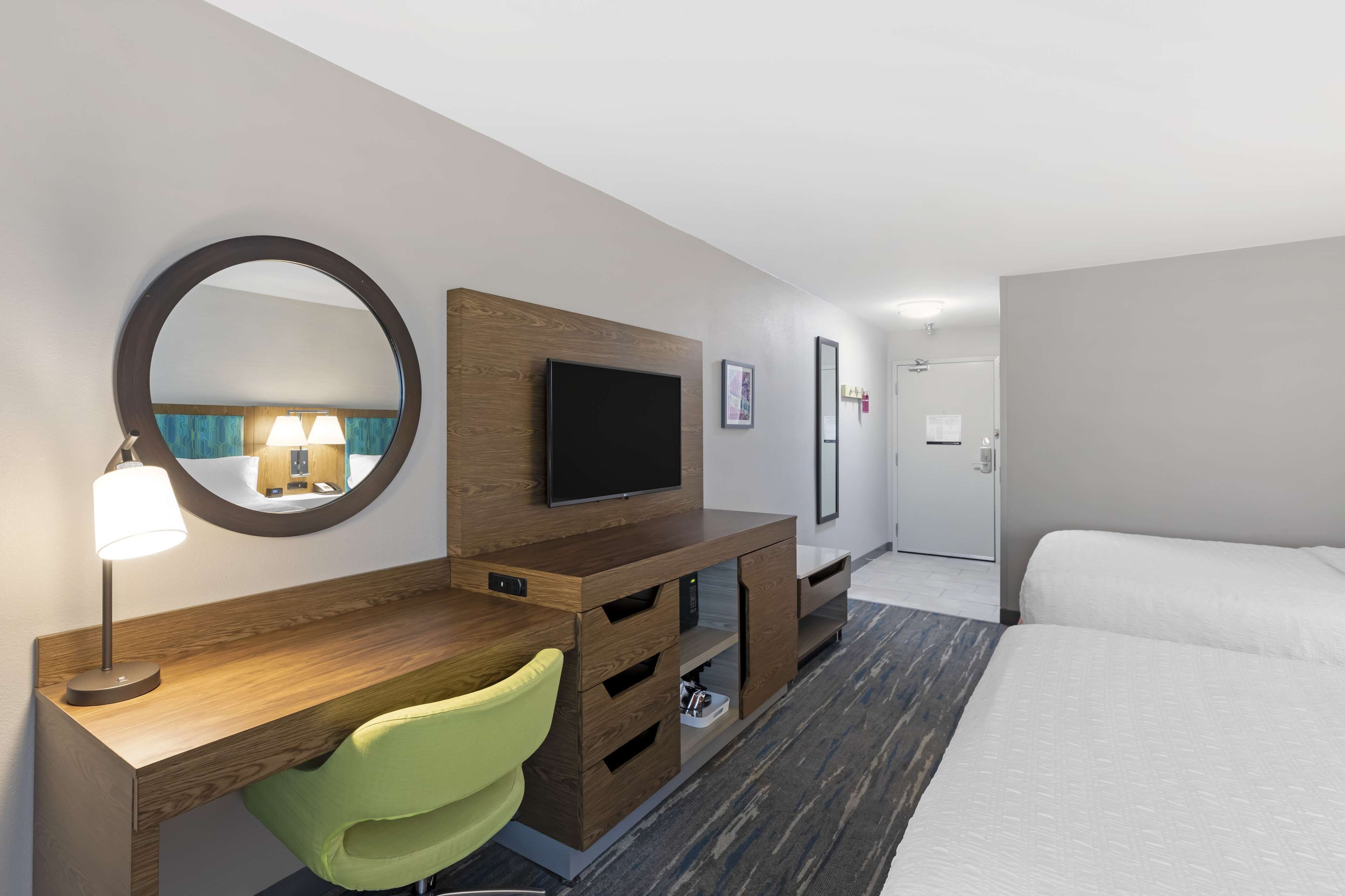 Hotellihuone, jossa on sänky, työpöytä tuolilla, televisio, peili ja lamppu.