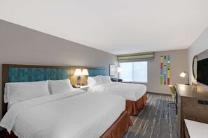 A hotel room with two beds, a desk, a TV, and a window.