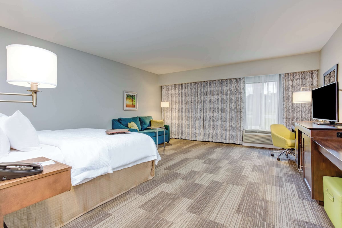 Ein Hotelzimmer mit einem Bett, einem Schreibtisch mit Fernseher, einem Sessel und einer Schreibtischlampe.