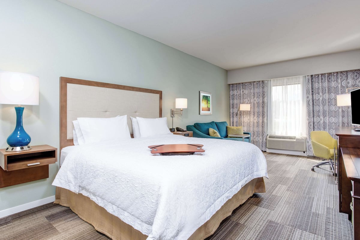 Ein Hotelzimmer mit einem großen Bett, einem Schreibtisch, einem Sessel, einem Nachttisch und einer Lampe.