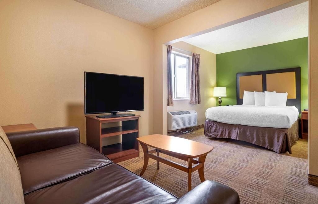 Une chambre d’hôtel avec un lit, une télévision, un canapé, une petite table et une fenêtre avec des rideaux.