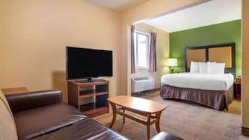 Une chambre d’hôtel avec un lit, une télévision, un canapé, une petite table et une fenêtre avec des rideaux.