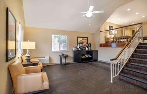 A spacious living area with a high ceiling, a fireplace, a staircase, and a ceiling fan. - Studio 6 Suites Jackson Ridgeland MS (Ridgeland)