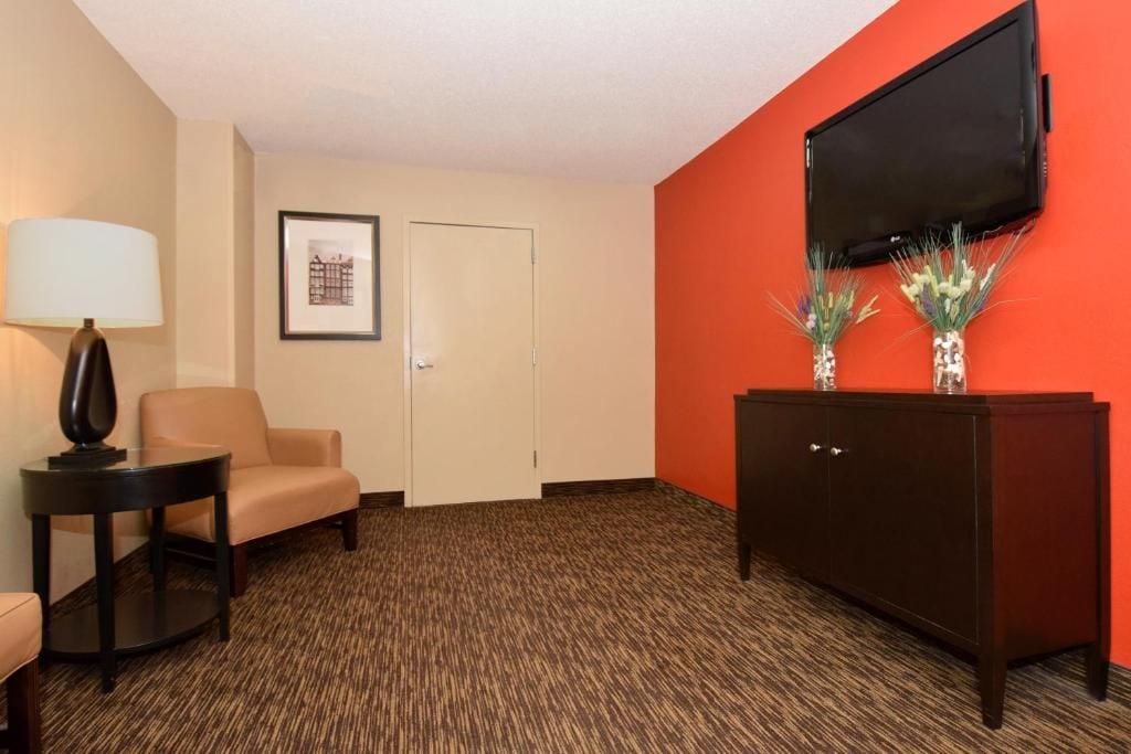A hotel room with a sofa, a small table with a lamp, a cabinet, and a flat-screen TV mounted on the wall.