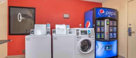 A laundry area with three washing machines and a Pepsi vending machine.
