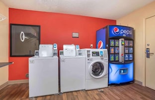 Un área de lavandería con tres lavadoras y una máquina expendedora de Pepsi.