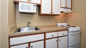 Une cuisine de taille réduite, avec des meubles blancs, un évier en acier inoxydable, un four à micro-ondes et une cuisinière.