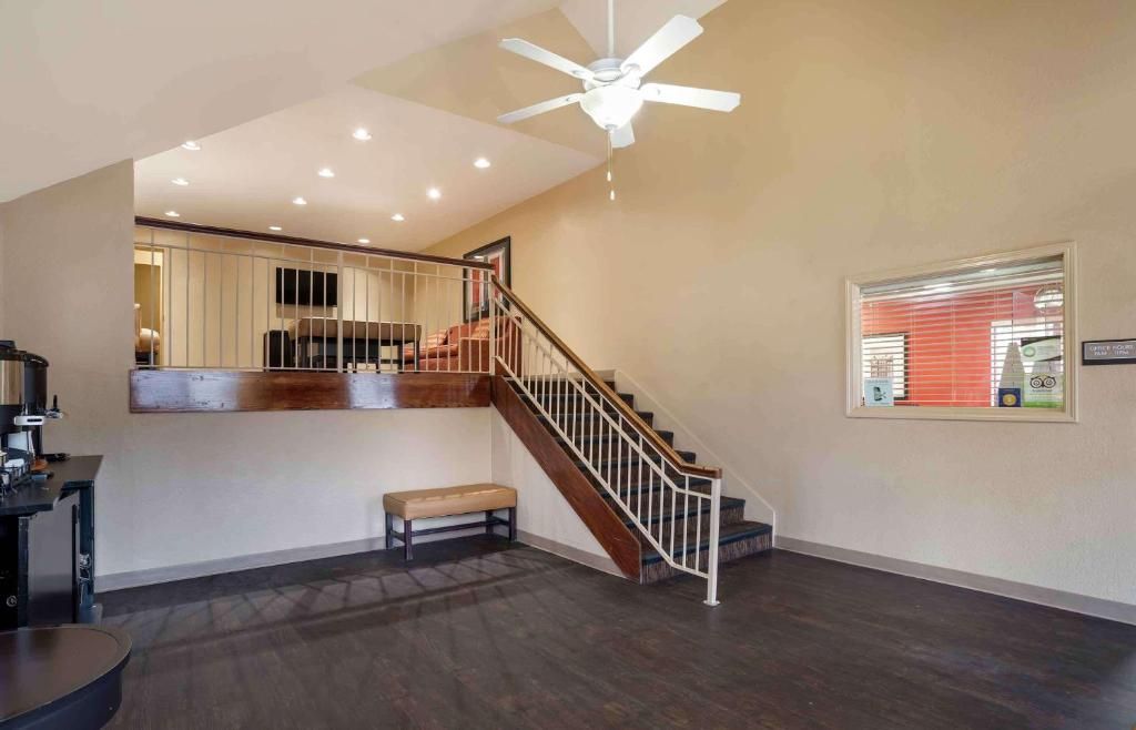 Una habitación amplia con una escalera, un ventilador de techo y una ventana con persianas.
