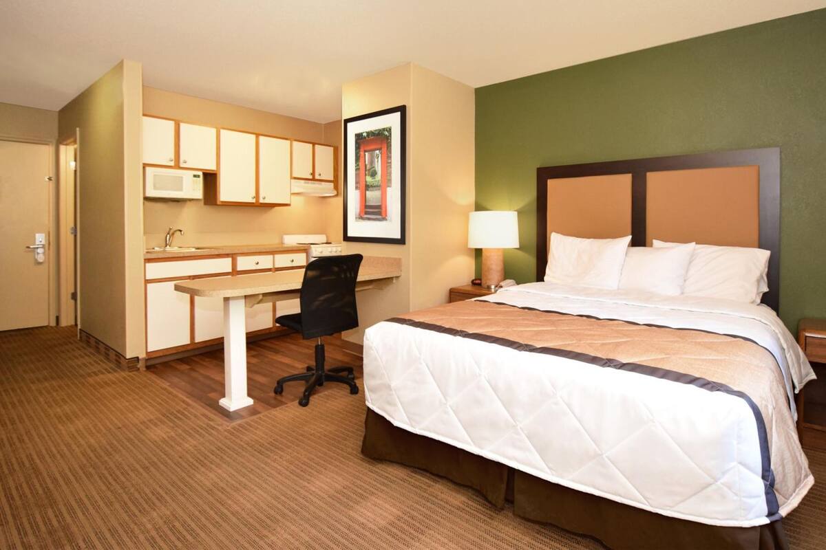 A hotel room with a bed, a desk with a chair, a microwave, and a framed picture on the wall.