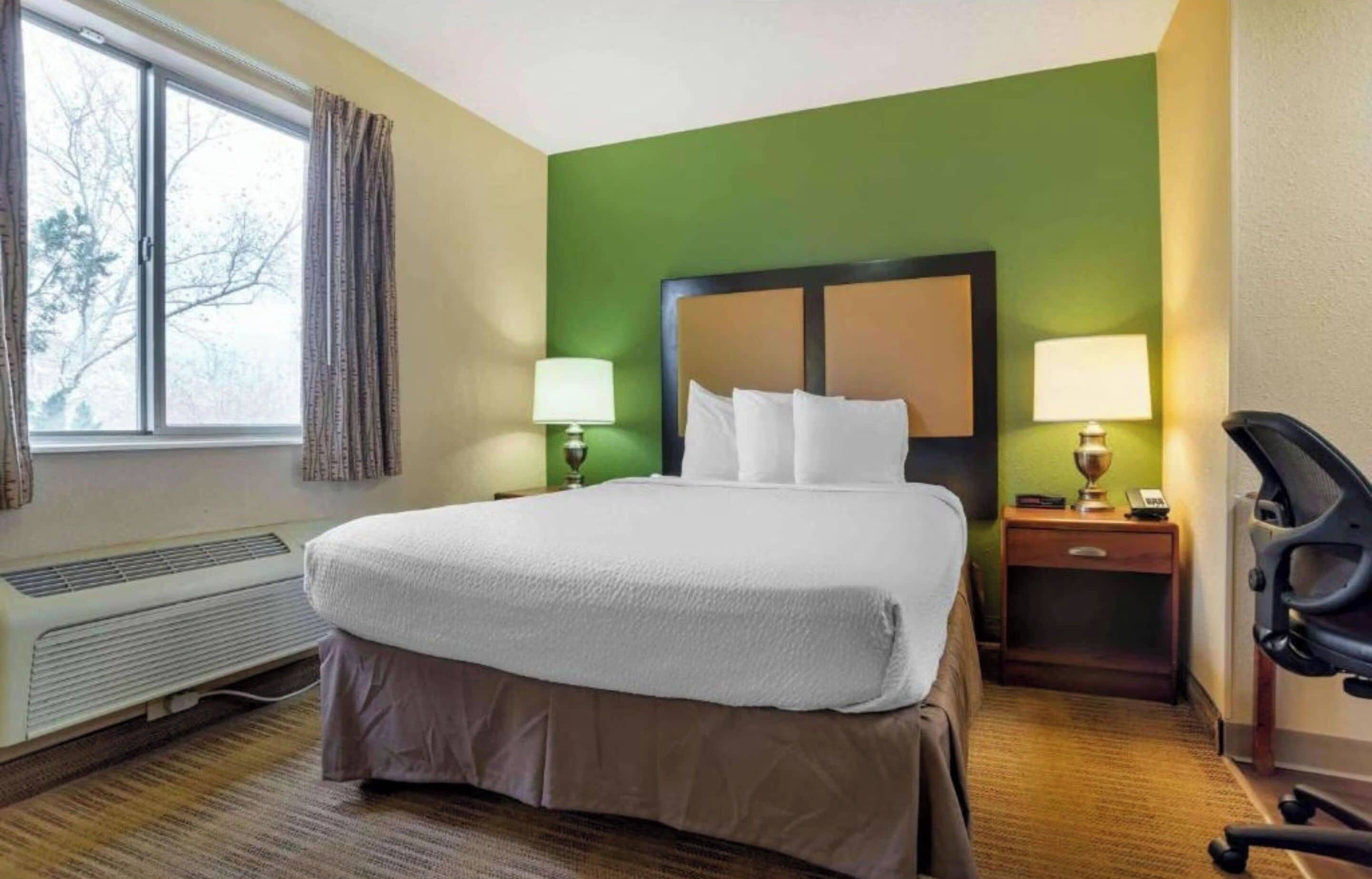 Une chambre d’hôtel avec un grand lit, deux lampes de chevet, un radiateur, un bureau avec une lampe et une chaise.