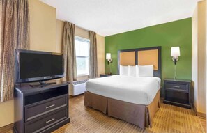 A hotel room with a bed, a TV, a heater, a nightstand, and a lamp. - Studio 6 Suites Jackson Ridgeland MS (Ridgeland)