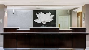 A reception desk with a large white lotus flower artwork above it, a white brick wall, and a green door in the background. - La Quinta Inn & Suites by Wyndham Macon (Macon)