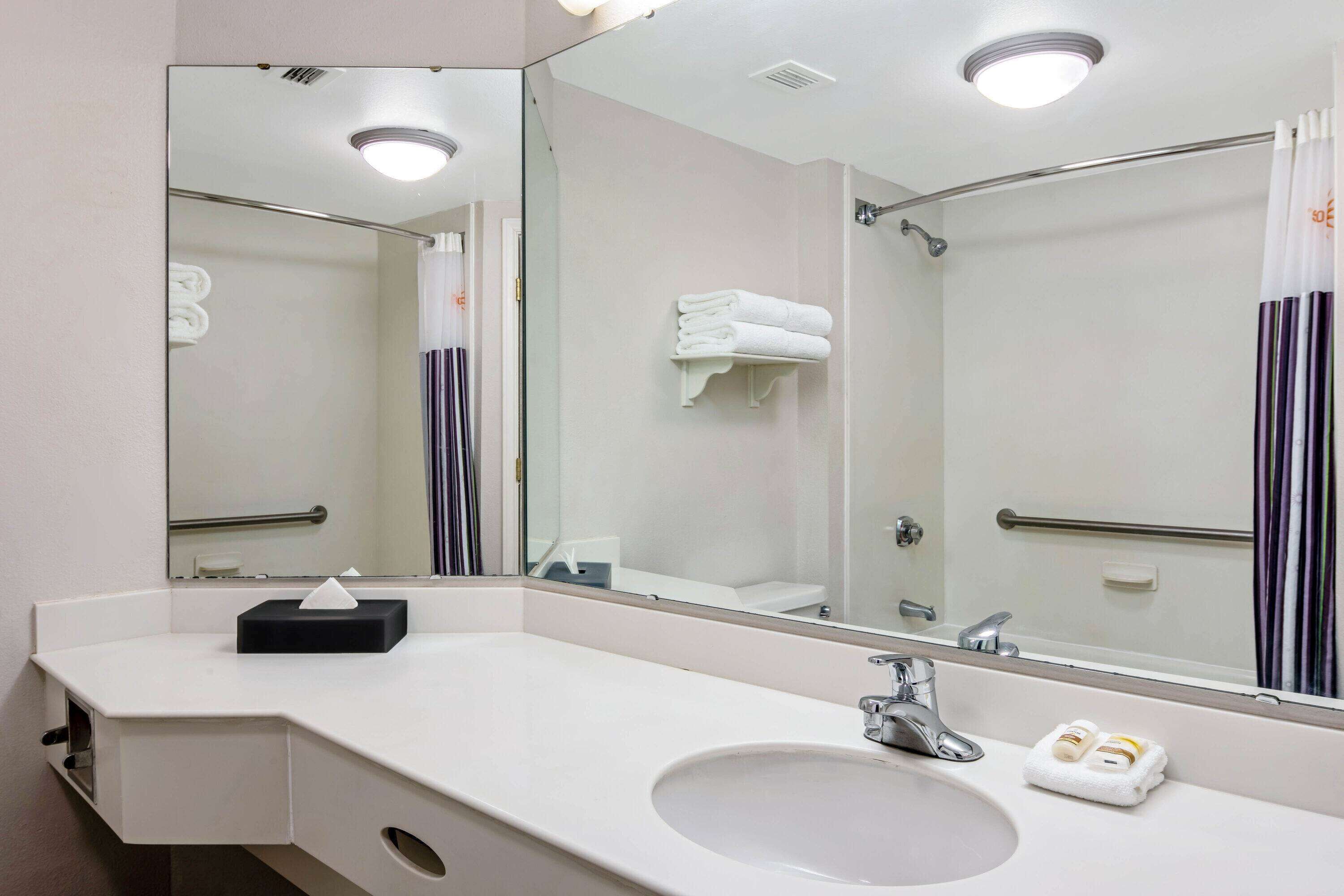 A hotel bathroom with a large mirror, a sink, a towel rack, and a shower area.