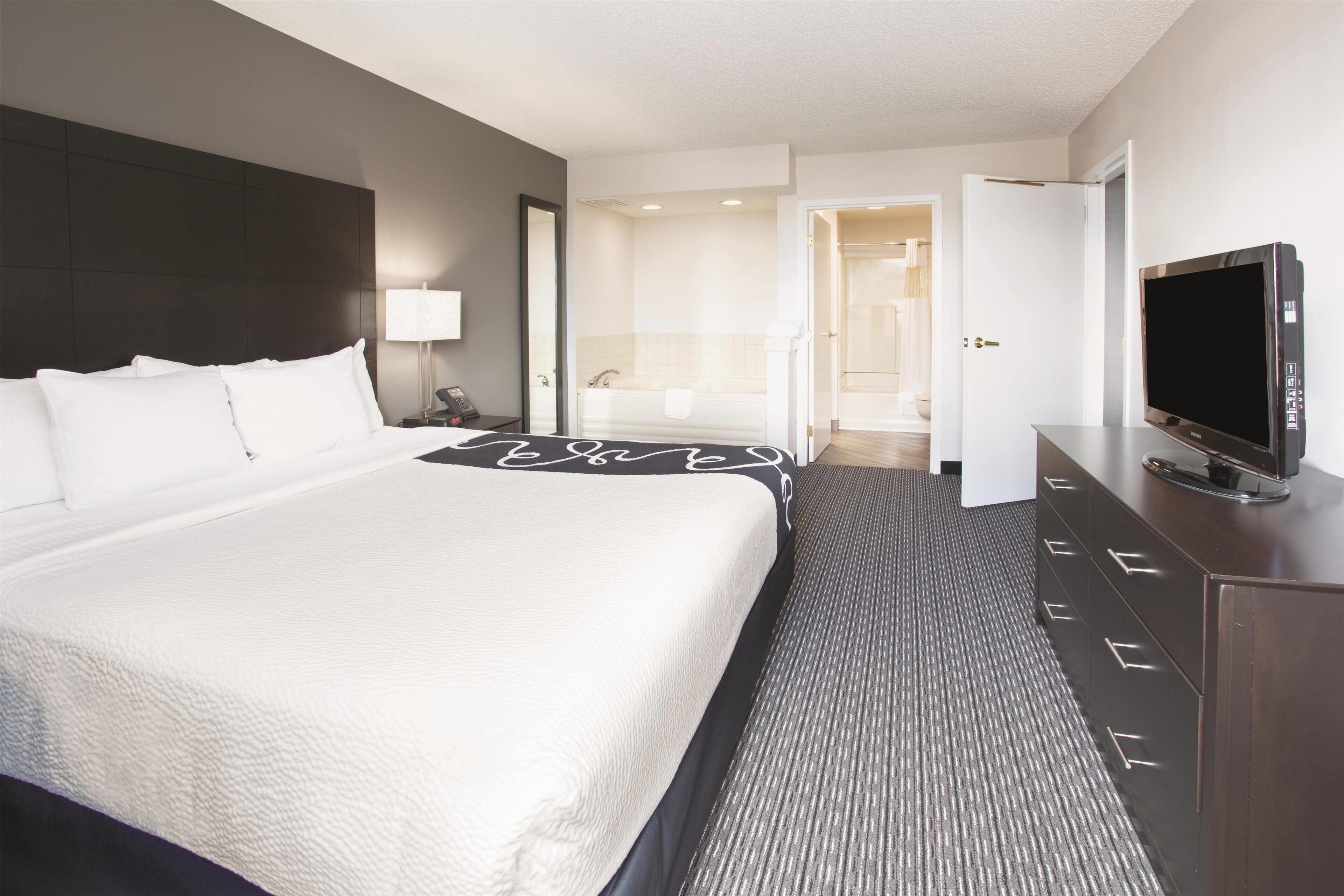 A hotel room with a large bed, a flat-screen TV, a dresser, and a bathroom visible through an open door.