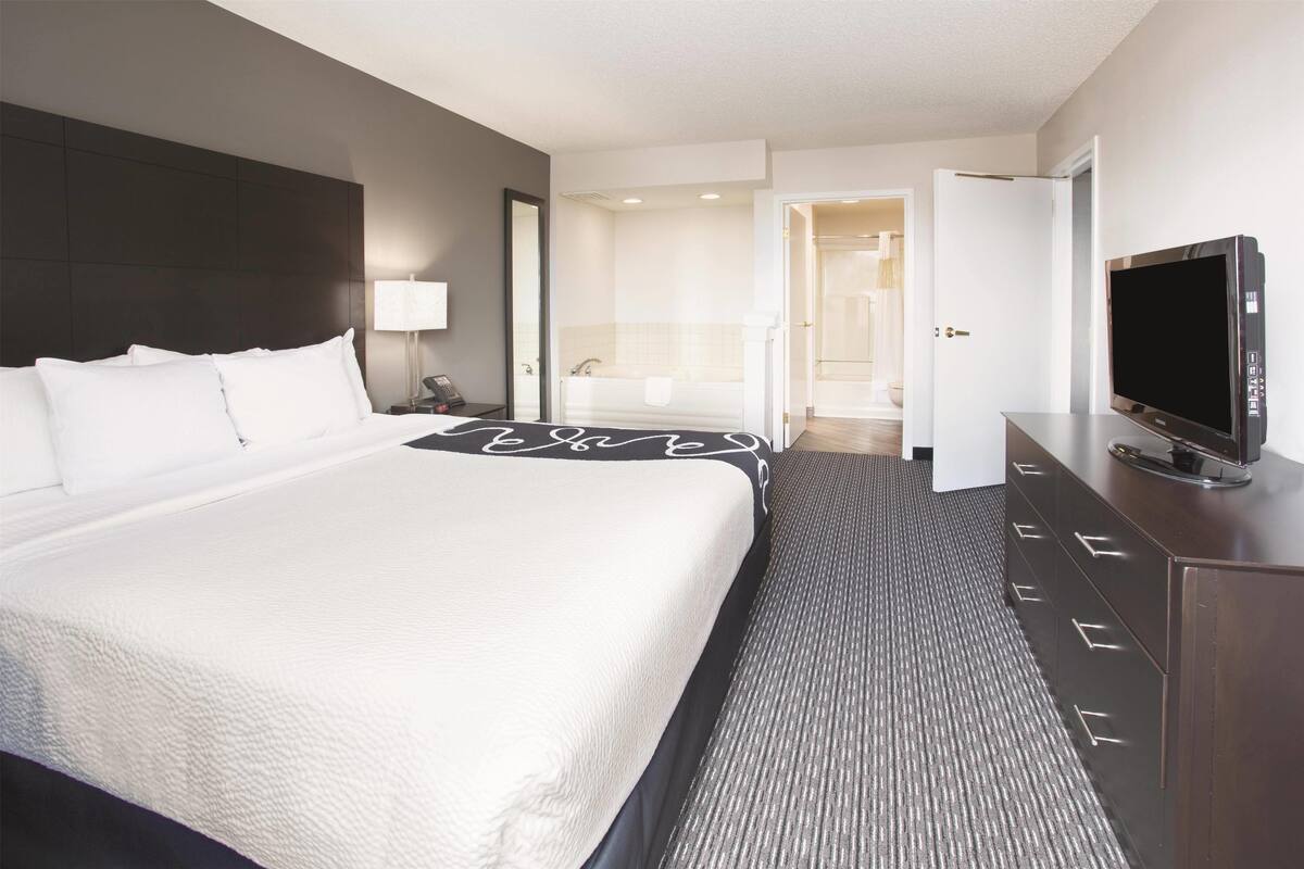 A hotel room with a large bed, a flat-screen TV, a dresser, and a bathroom visible through an open door.