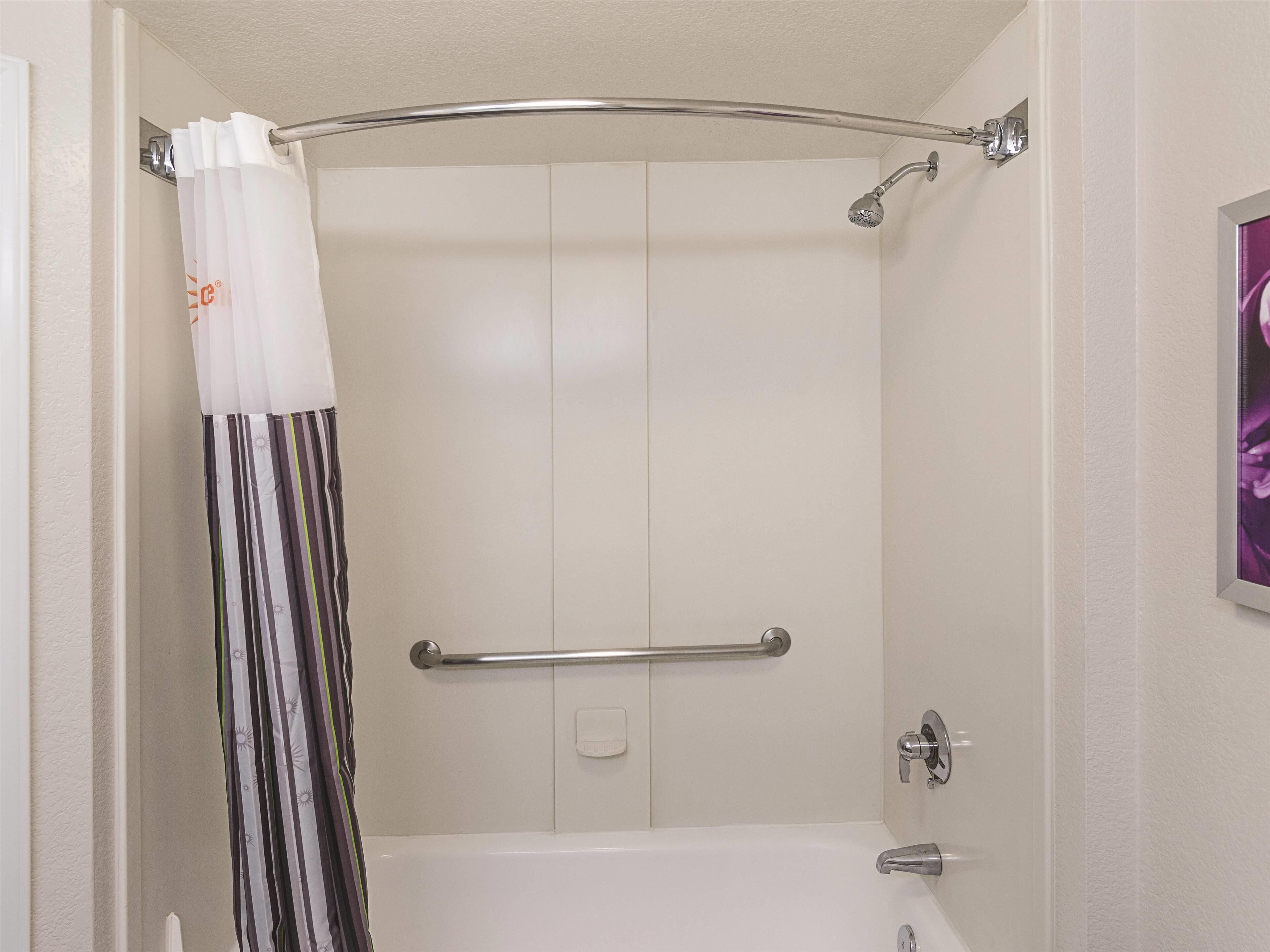 A shower area with a white bathtub, a shower curtain, and a handrail.