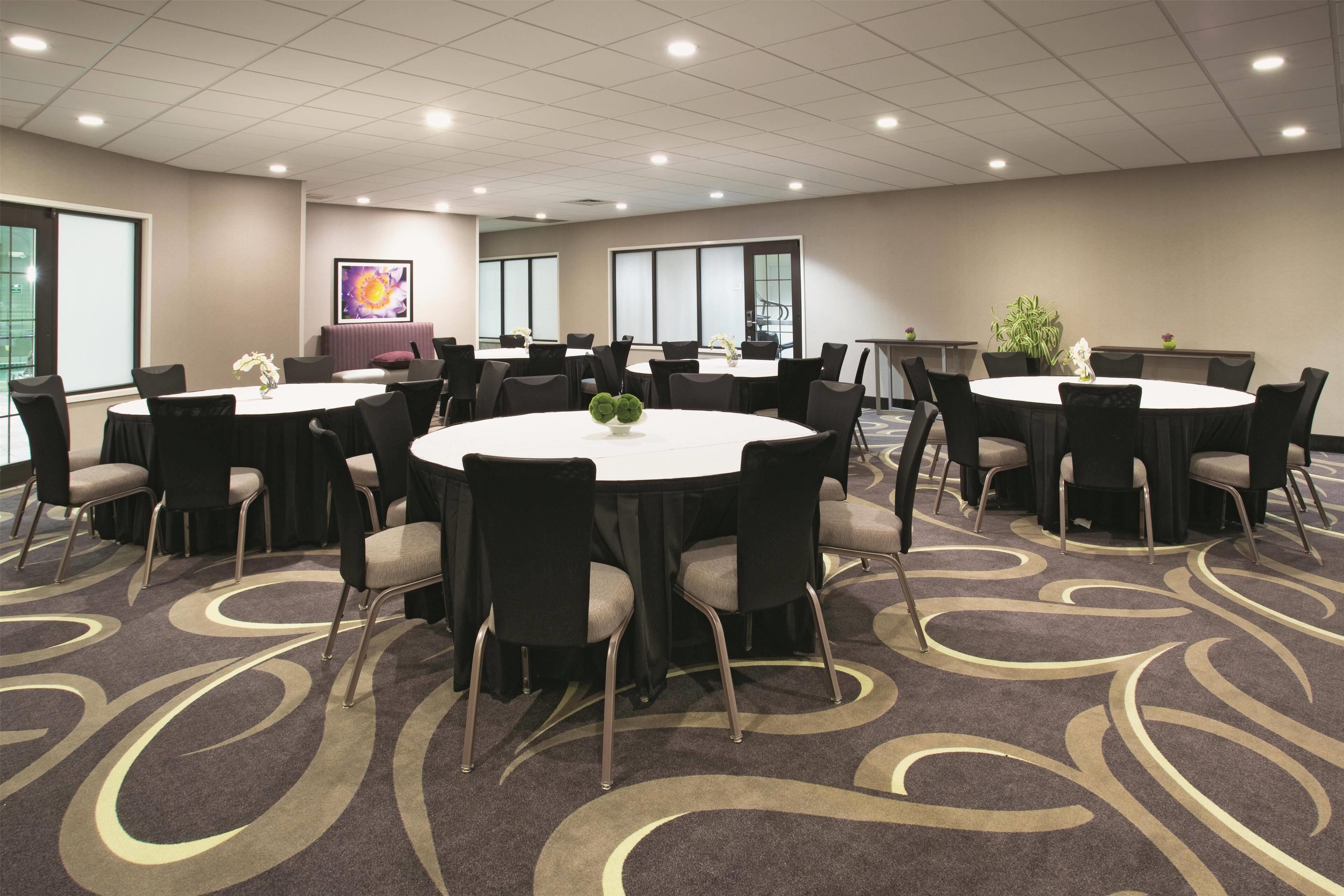 A conference room with multiple round tables, black chairs, and a patterned carpet.