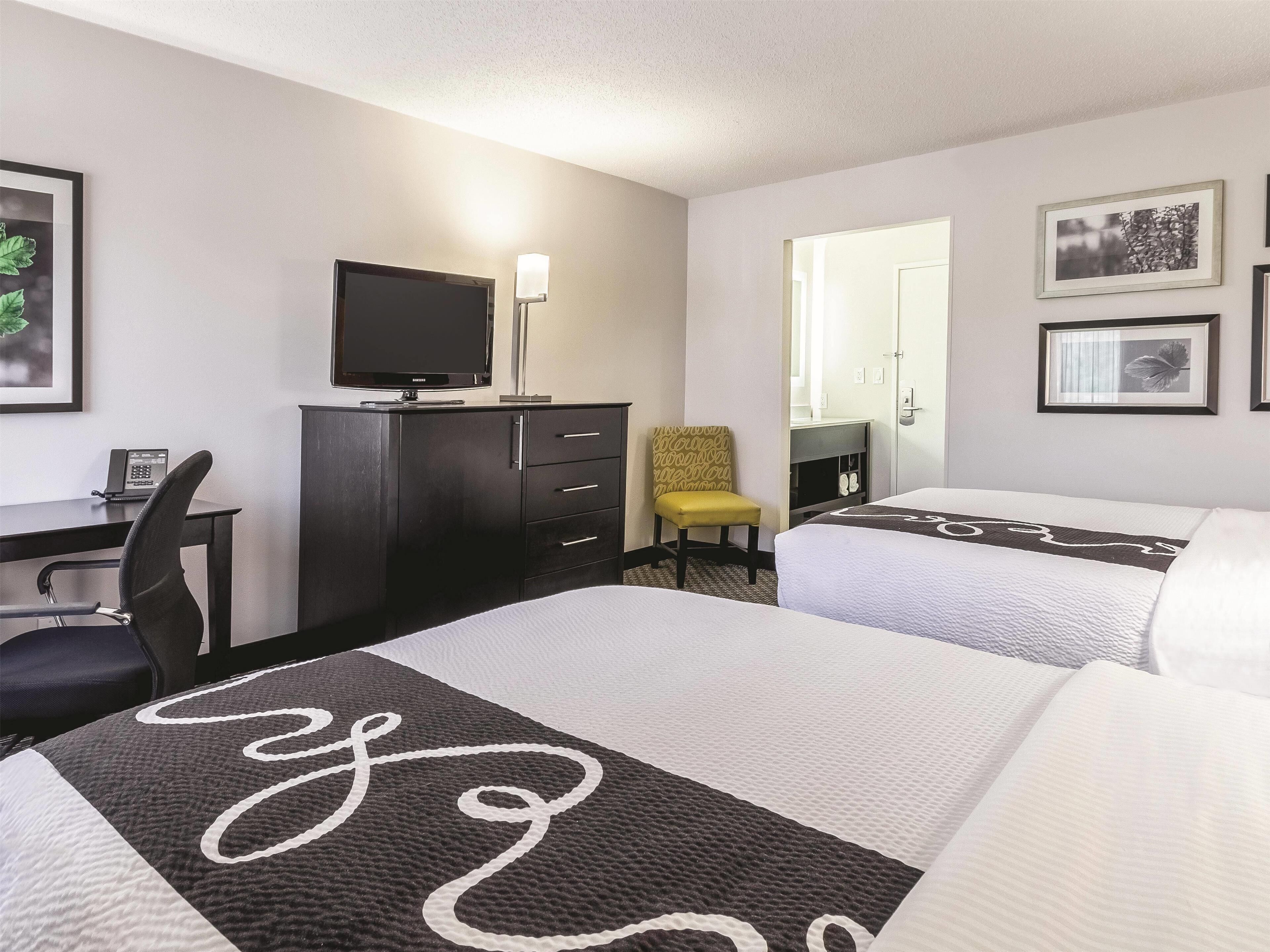 A hotel room with two beds, a desk with a computer and phone, a chair, and a TV.