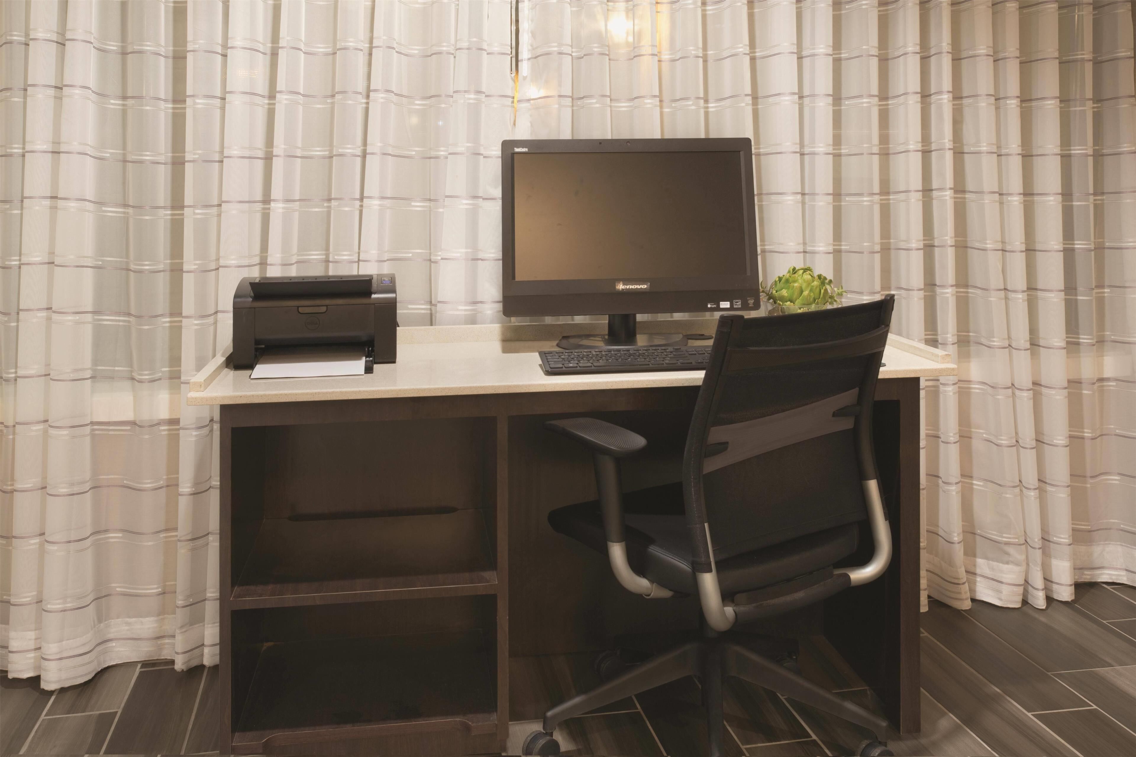 A wooden desk with a computer, a printer, and a chair.