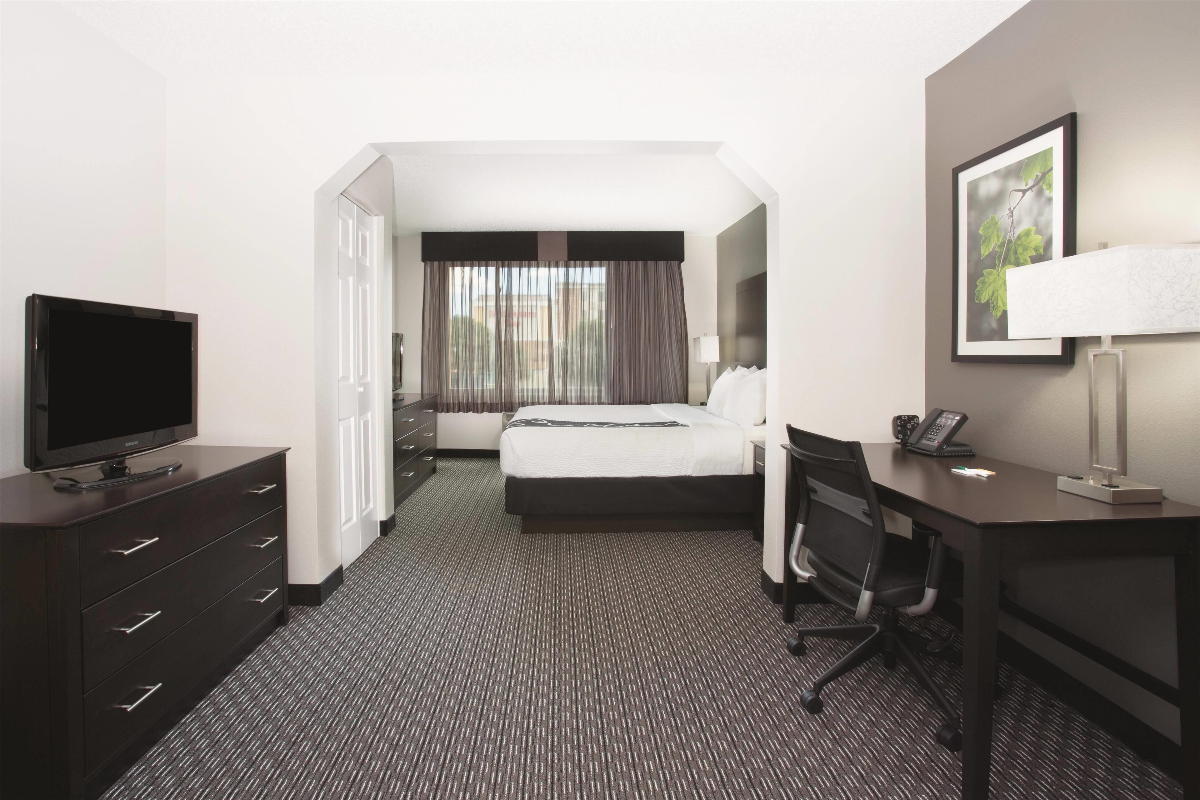 A hotel room with a bed, a desk, a chair, a TV, a phone, and a window with curtains.