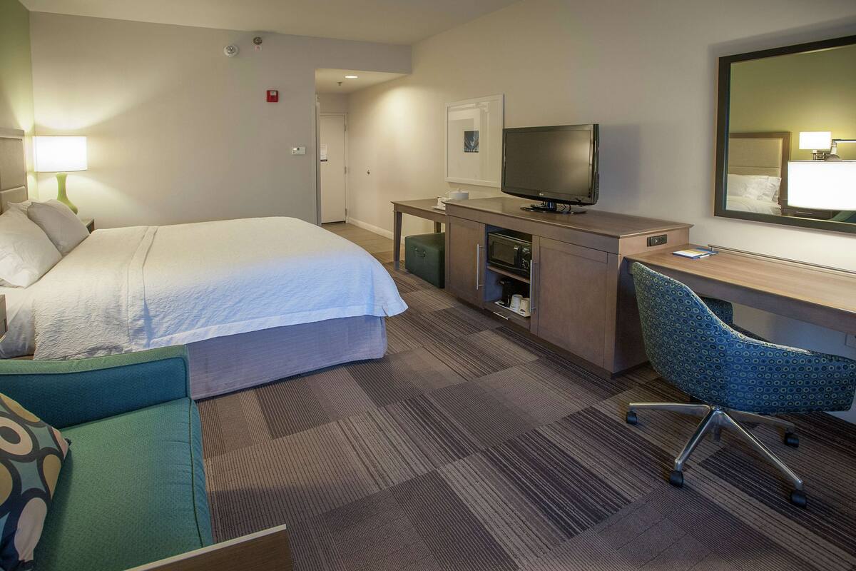 A hotel room with a bed, a desk, a television, and a chair.